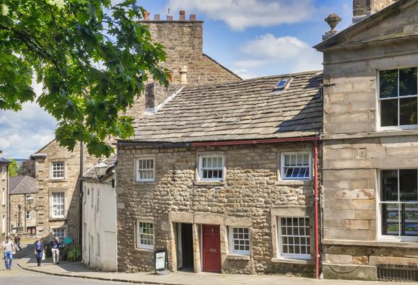 Photo of the Cottage museum: a small two-storey stone building in a row of other buildings in various styles on a steep cobbled street..